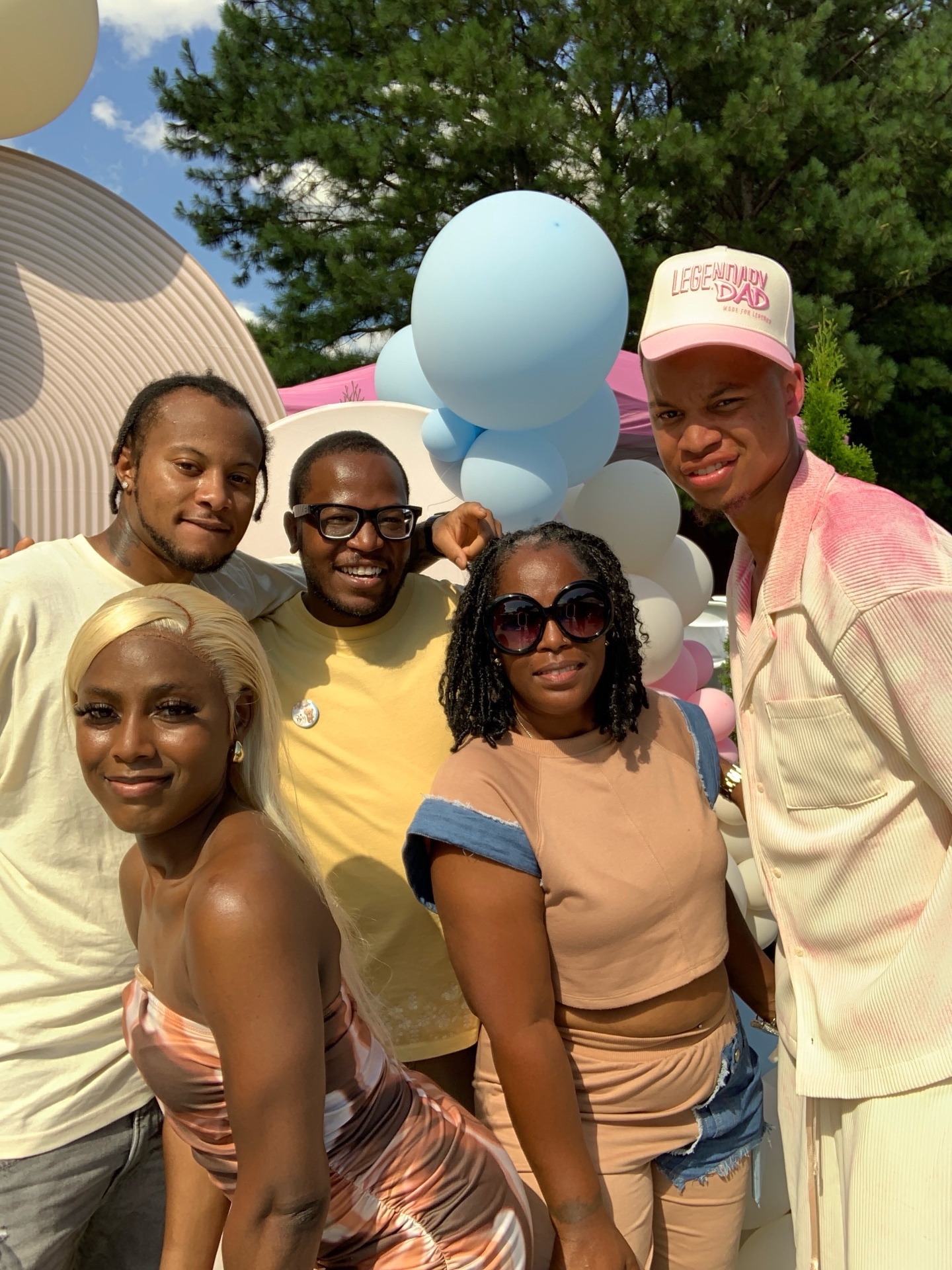 Group of friends posing at an outdoor baby shower photo booth with a balloon arch
